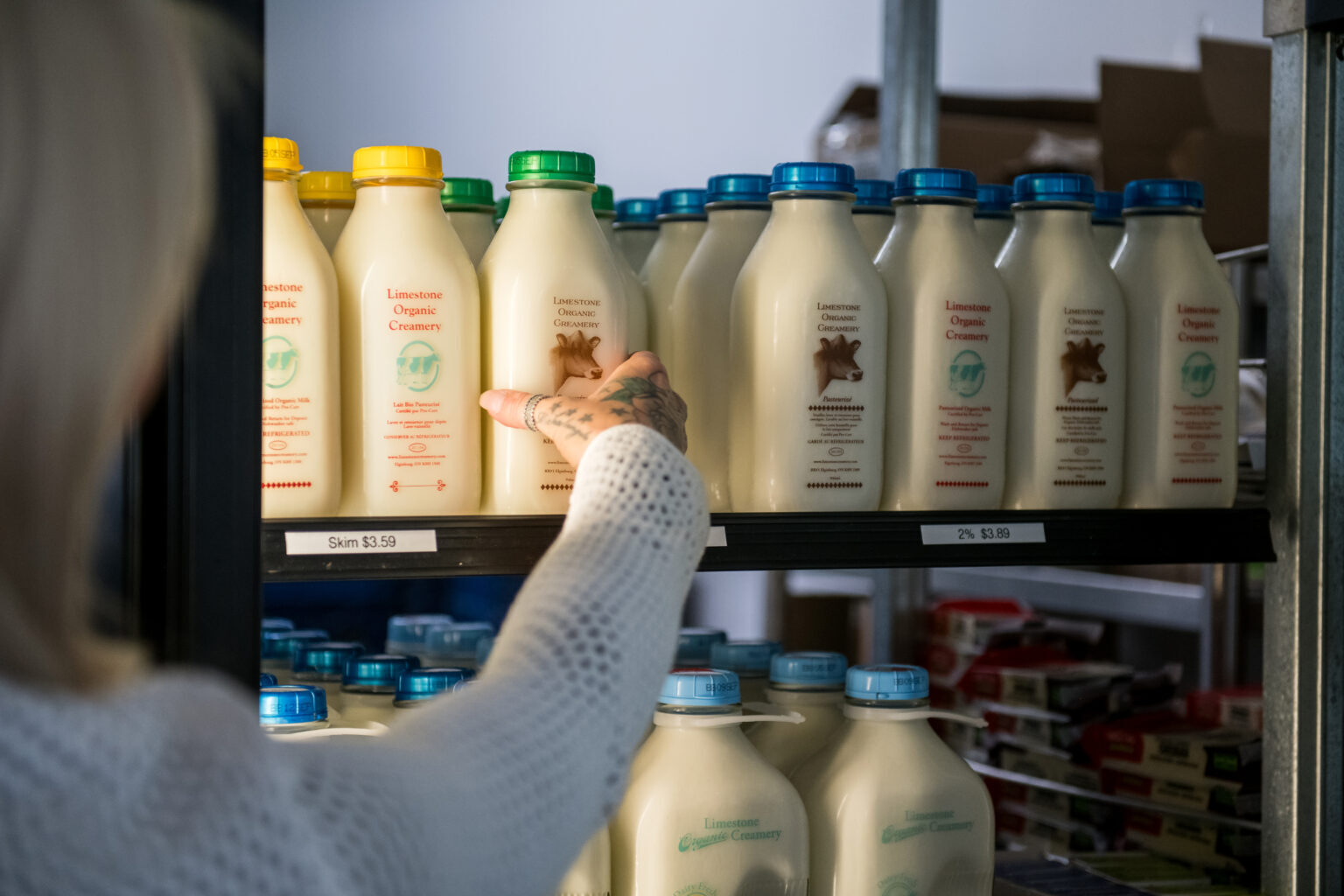 A woman getting a bottle of Limestone City Creamery milk from a fridge stocked with Limestone Creamery products.