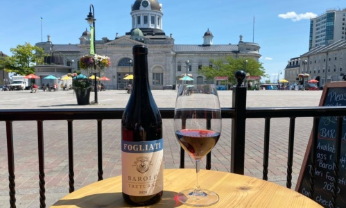 A wine bottle and a glass of wine on top of a table outside Bobbi Pecorino's, with Springer Market Square in the background.
