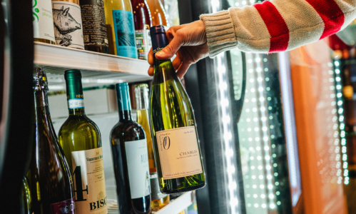 A person taking a wine bottle out of a fridge filled with different wines.