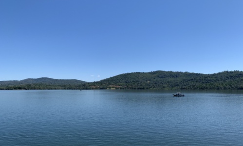 A view of the Collins Lake, with rolling hills behind and a boat cruising through the water.