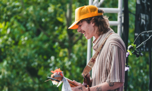 Nolan Hubbard performing live on a stage with green foliage behind him.