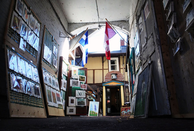 A variety of prints, paintings, and postcards are hung in the alleyway. The cases close at night to look like French windows.