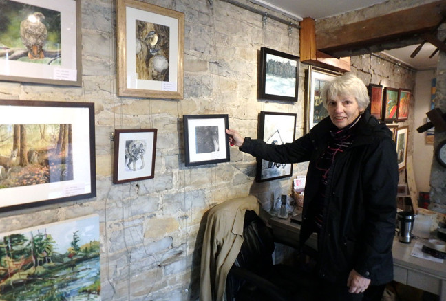 Chris Perry stands with her graphite drawing of a raven, whose curious, intelligent eye draws attention from viewers.