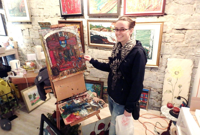 Queens student Elizabeth Gibson Crowder stands next to a painting-in-progress by David Dossett.